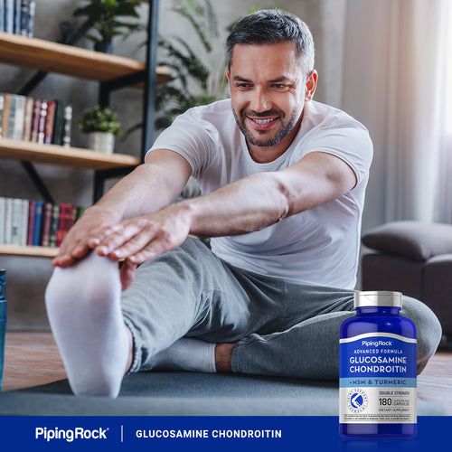 Man stretching in a living room with a bottle of Piping Rock Glucosamine Chondroitin supplement.