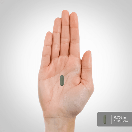Hand holding a small green pill with measurements on a gray background